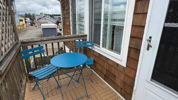 A wooden deck with a blue table and chairs, a white door, and a view of a street.