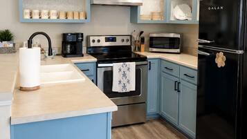 A modern kitchen with light blue cabinetry, stainless steel appliances, and a black refrigerator.