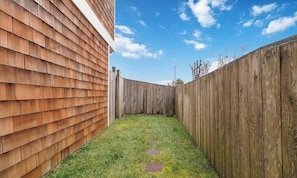 A narrow backyard with a wooden fence, a grassy area, and a clear sky. - Rest Ashored- 2 mins from the beach, dog friendly (Long Beach)