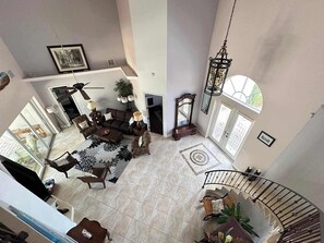 A spacious living area with a high ceiling, a dining table, multiple chairs, a sofa, a staircase, and a large window. - Villa Memories - Cape Coral (Cape Coral)