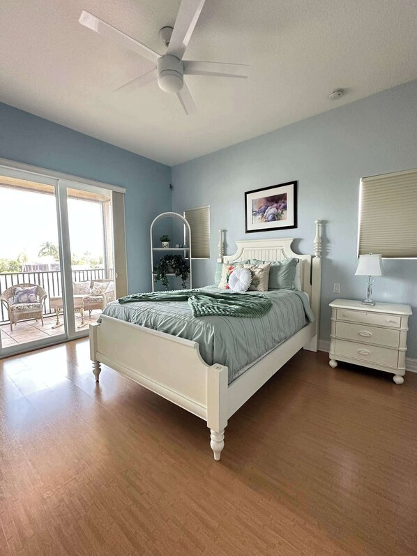 A bedroom with a bed, a nightstand, a lamp, a ceiling fan, a window with blinds, and a view of the outdoors. - Villa Memories - Cape Coral (Cape Coral)