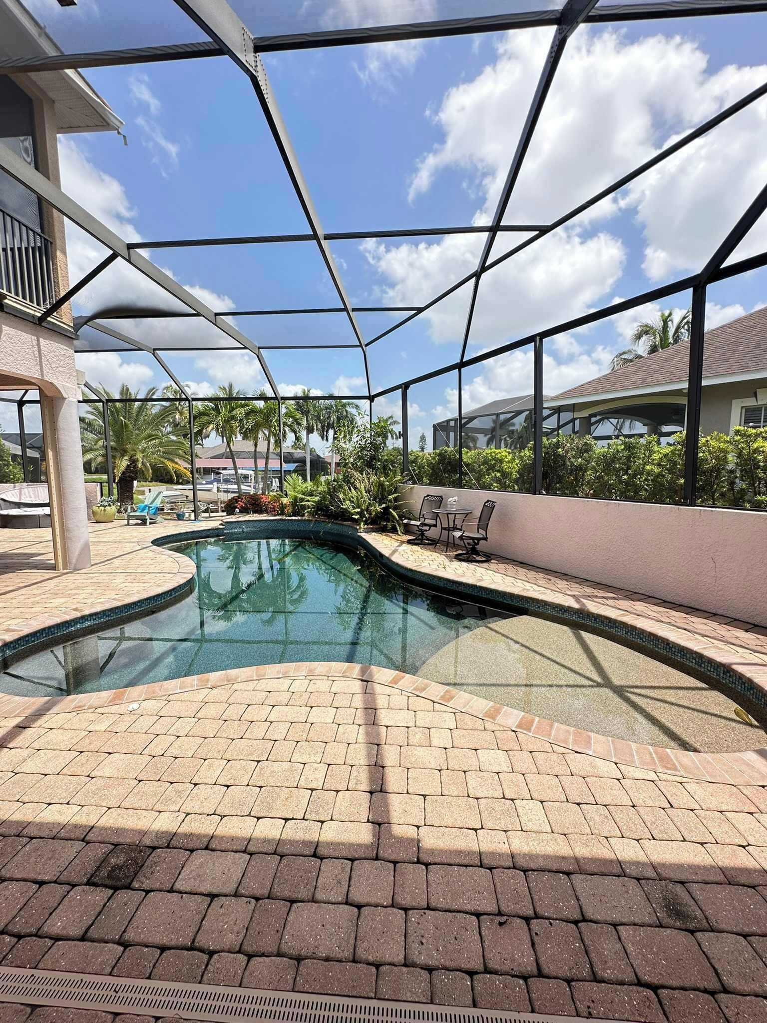 An indoor swimming pool with a clear glass ceiling, surrounded by lounge chairs and a brick floor.