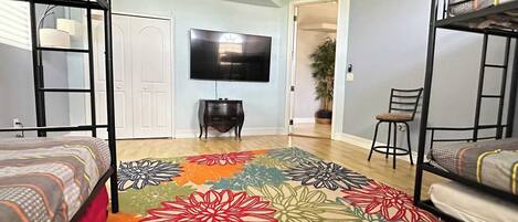 Une chambre de dortoir avec des lits superposés, un téléviseur à écran plat, un bureau et un tapis à motifs floraux aux couleurs vives.