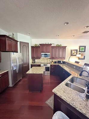 A modern kitchen with a stainless steel refrigerator, double ovens, a microwave, and granite countertops. - Villa Memories - Cape Coral (Cape Coral)