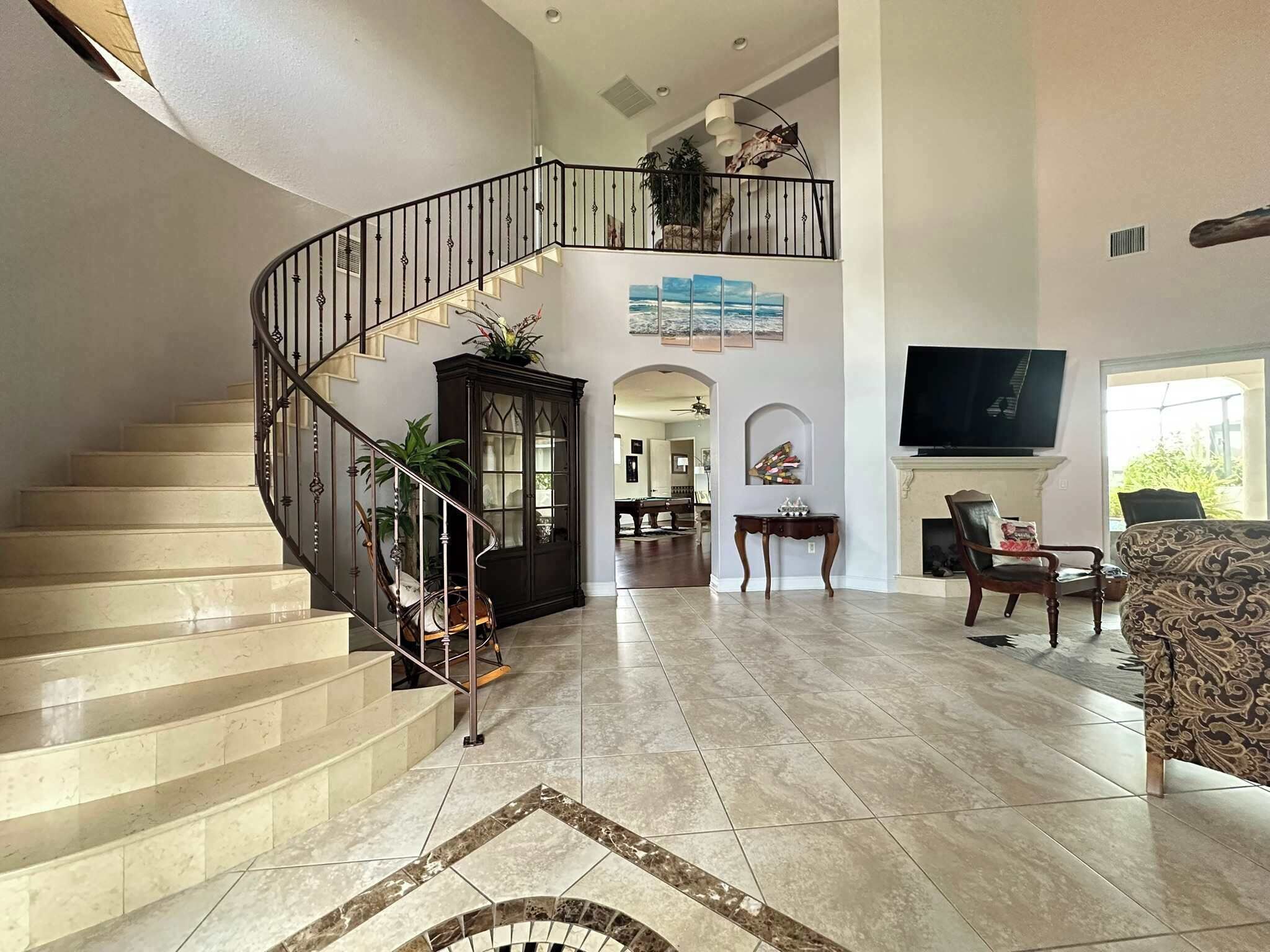 A spacious living area with a curved staircase, a flat-screen TV, and a fireplace.