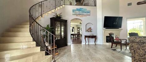 A spacious living area with a curved staircase, a flat-screen TV, and a fireplace.