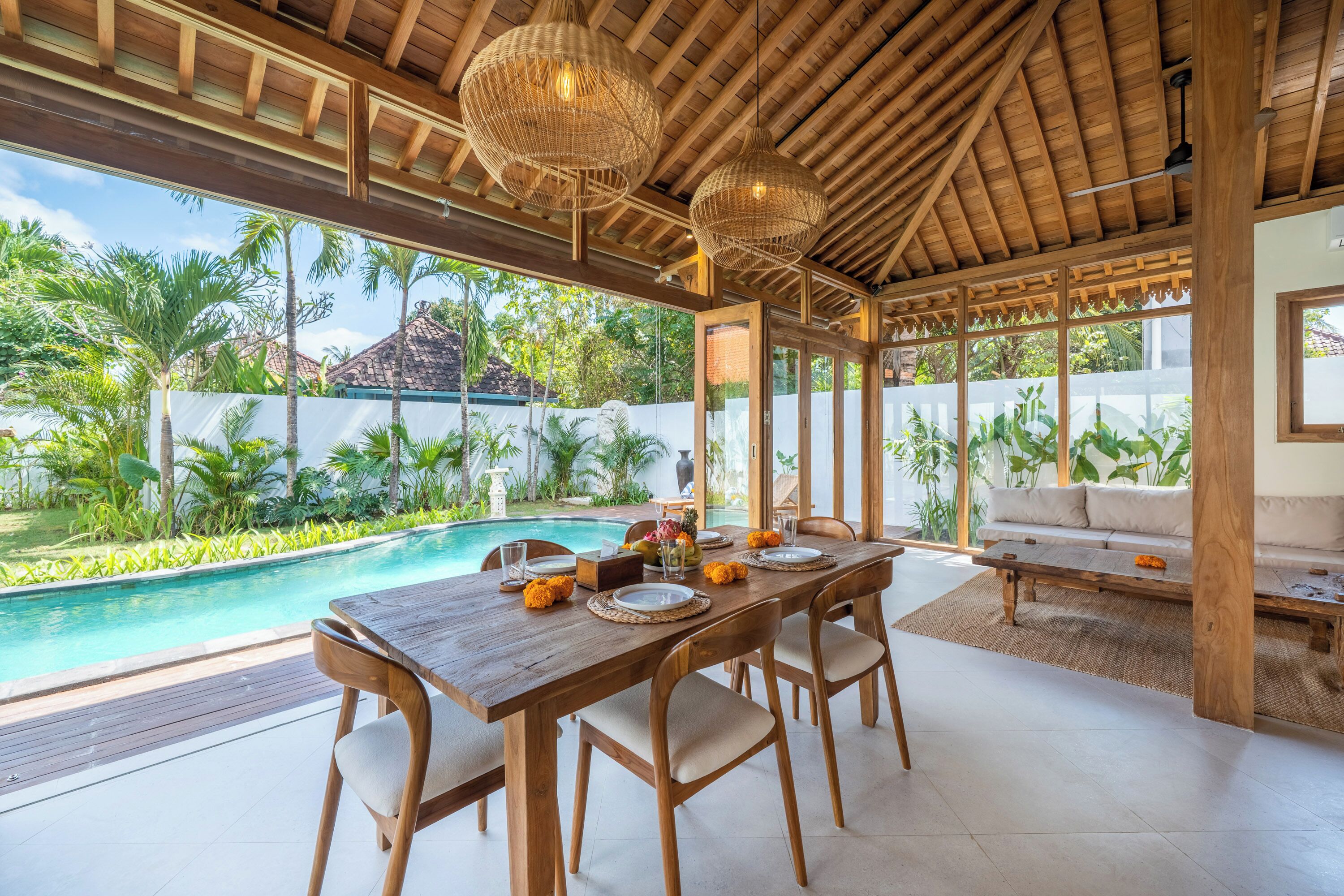 An outdoor dining area with a pool, wooden furniture, and a view of a tropical landscape.