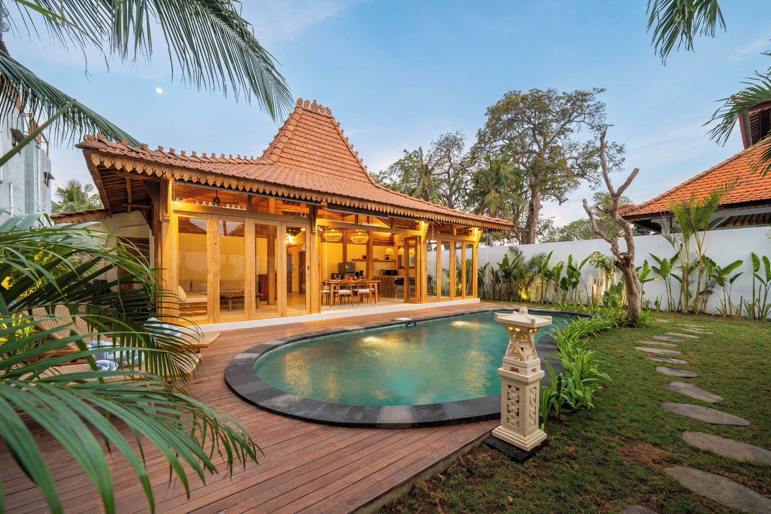 A traditional-style building with a tiled roof, a swimming pool, and a garden with tropical plants.