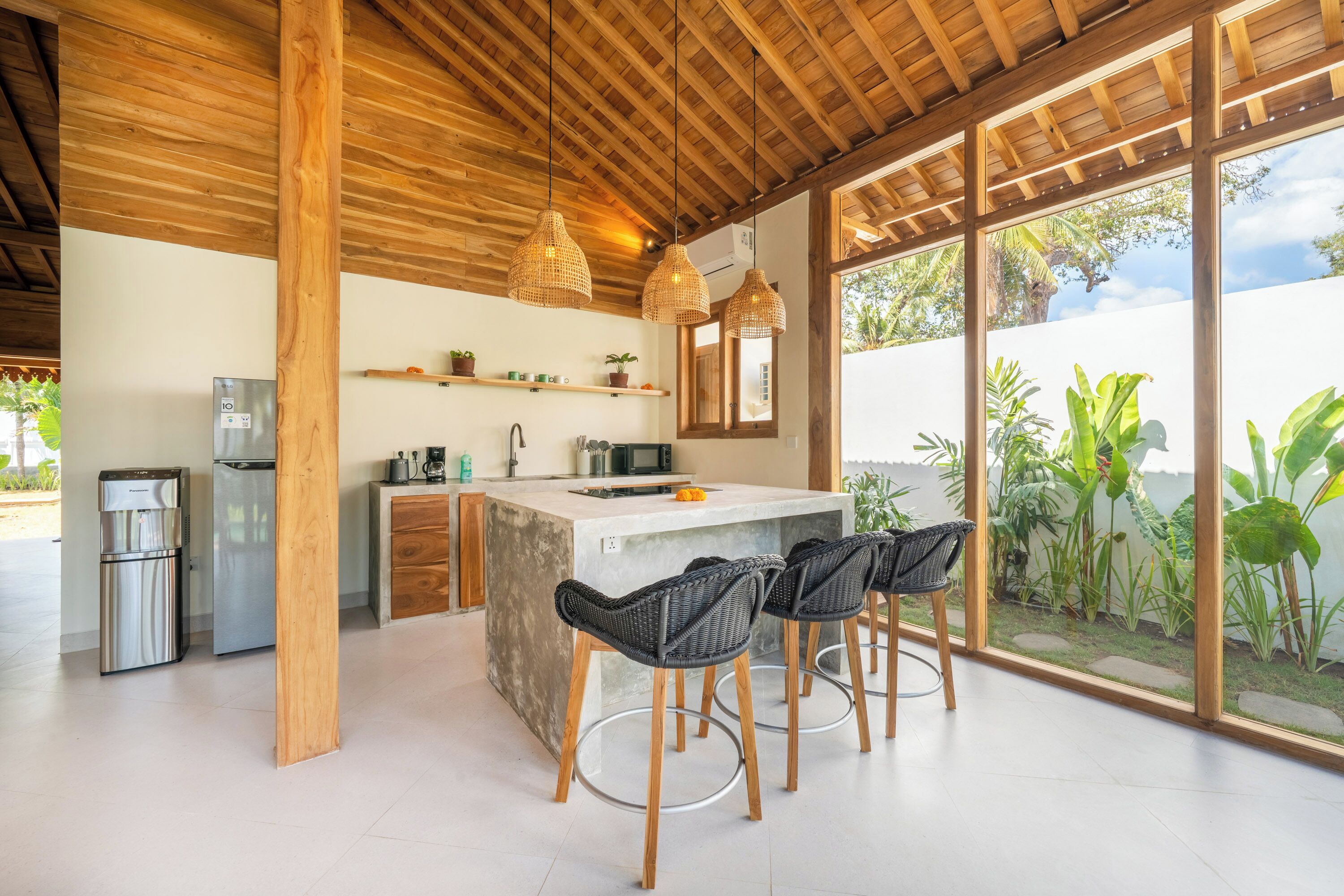A modern kitchen with a central island, bar stools, and a view of the garden through large windows.