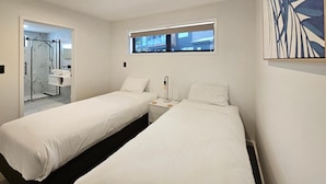 Une chambre d’hôtel avec deux lits, une fenêtre, une salle de bain avec une porte en verre et un tableau au mur.