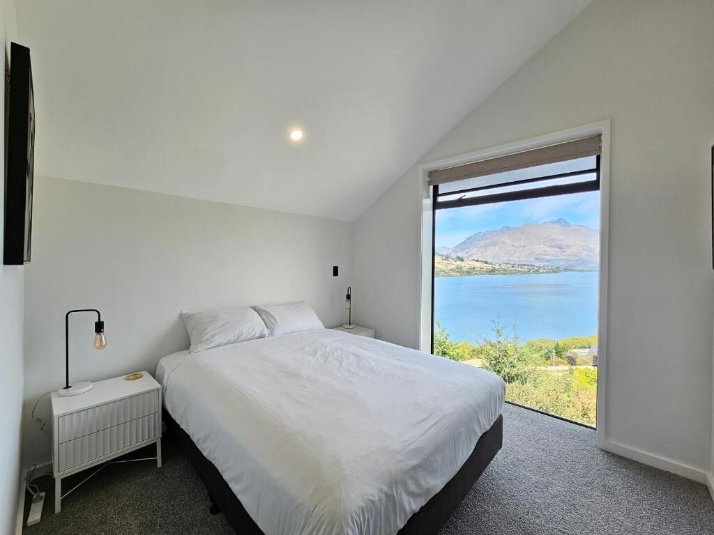A bedroom with a large bed, a nightstand, a lamp, and a view of a lake.