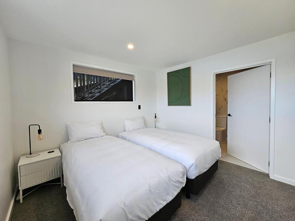 A bedroom with two beds, a nightstand, a radiator, a picture on the wall, and a door leading to another room.