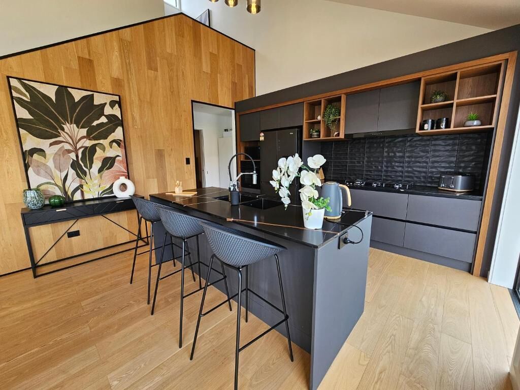 Cozinha moderna com ilha central, banquetas e painel de fundo preto.