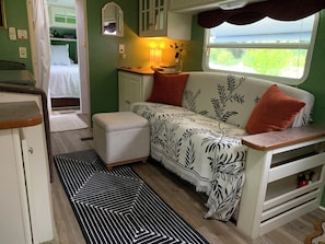 A compact RV interior with a kitchenette, a sofa with patterned upholstery, and a window with a view.