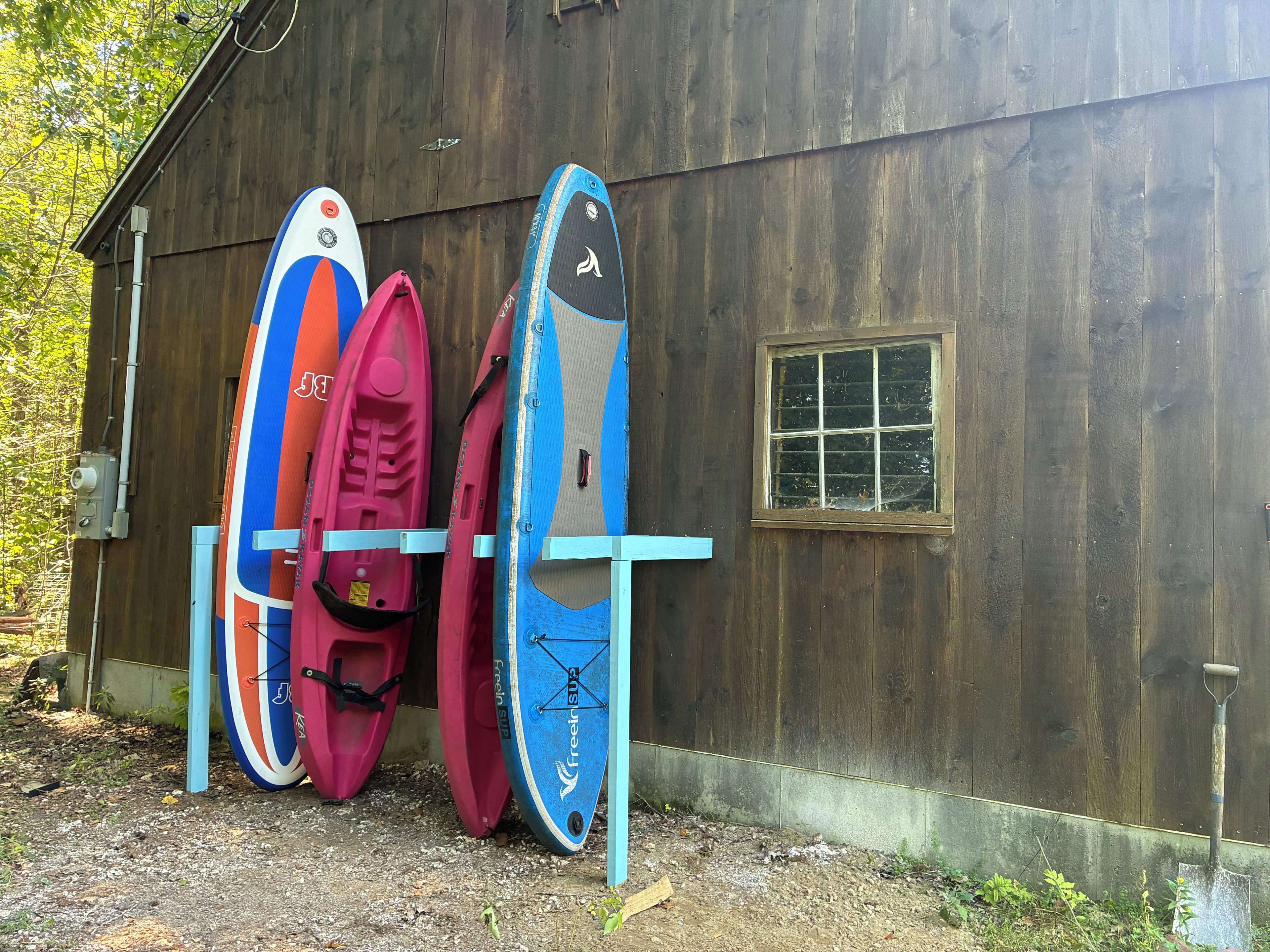 Kayaks and a shovel leaning against a wooden shed.