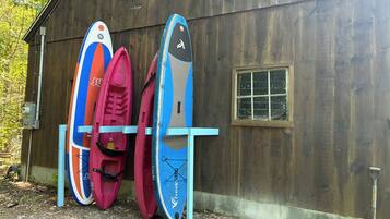 Kayaks and a shovel leaning against a wooden shed.