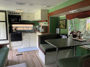 Una cucina compatta per camper con fornello, lavello e pensili, una zona pranzo con una panca e una finestra vista verde.