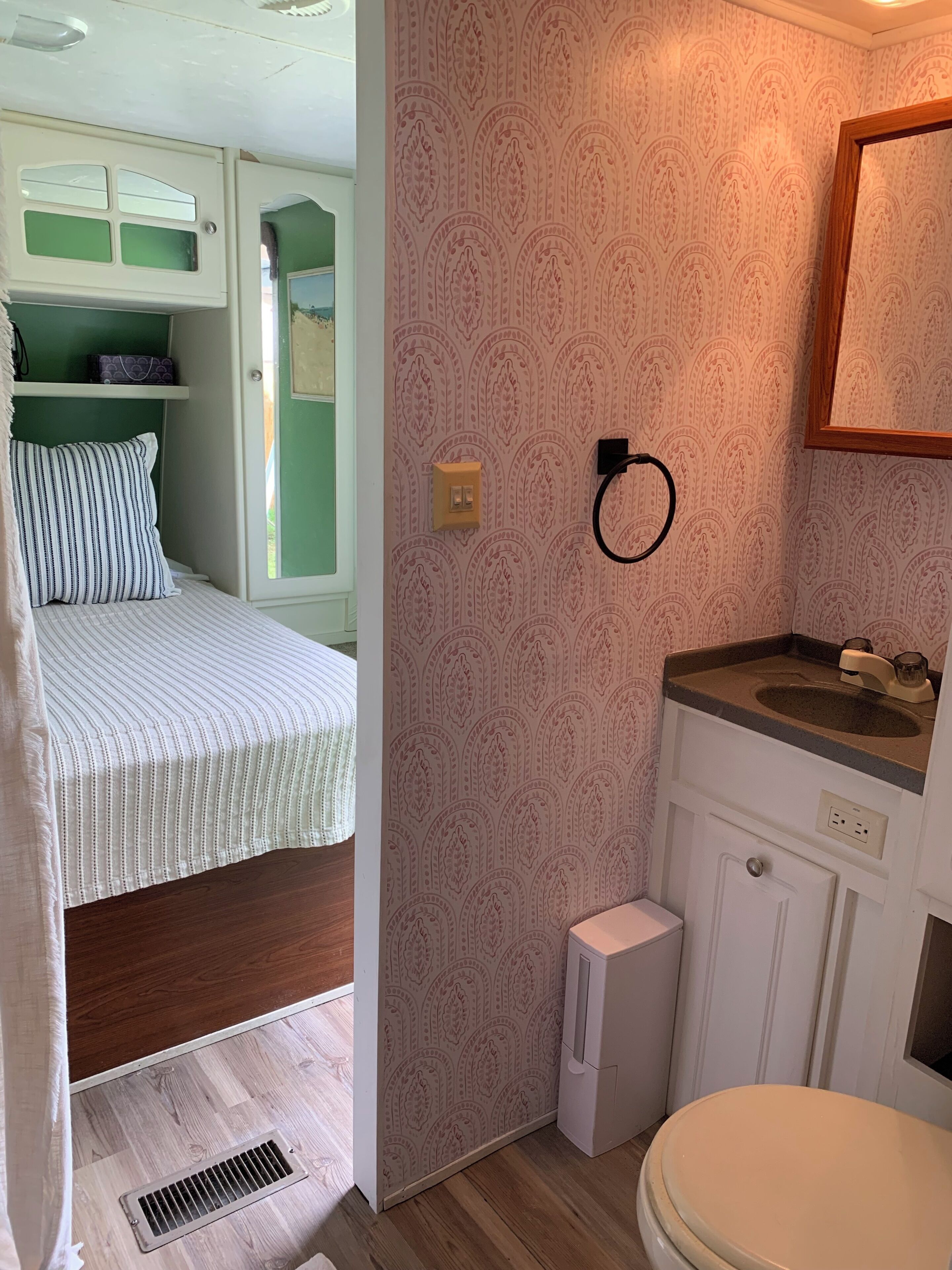 A compact room with a bed, a small white toilet, a sink, and a window.