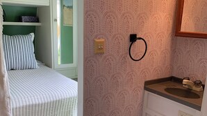 Quarto compacto com cama, um sanitário pequeno e branco, pia e janela.