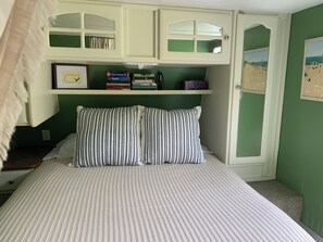 A bedroom with a bed, striped bedding, a bookshelf with books, and a framed picture on the wall.