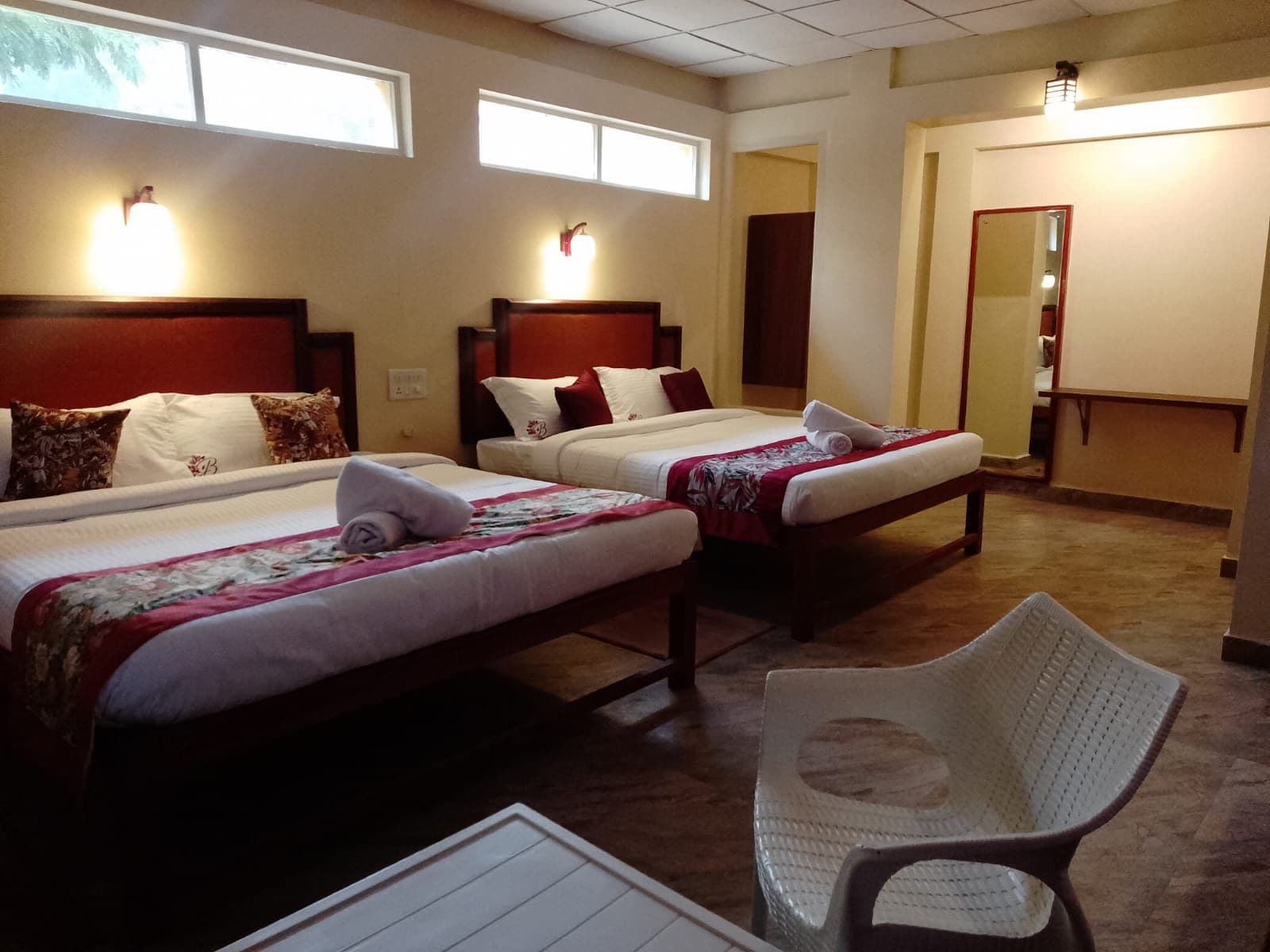 A hotel room with two beds, a chair, and a mirror.