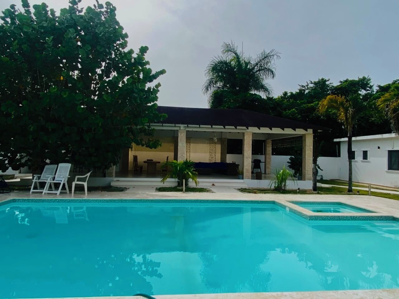 Une piscine avec des chaises longues, un patio couvert et un bâtiment doté d’un toit plat.
