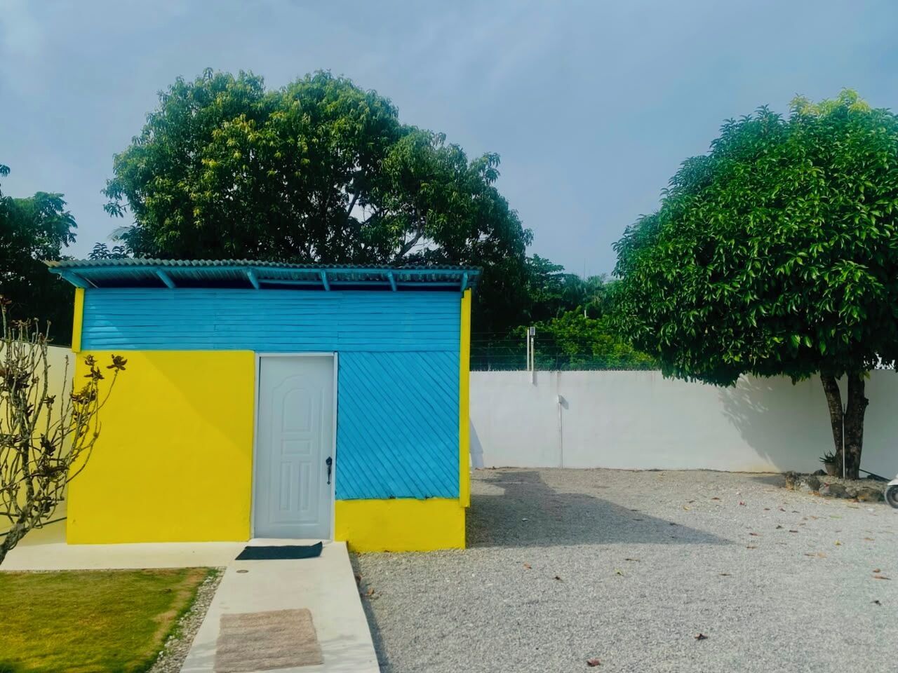 Ein kleines, einstöckiges Gebäude mit blauer und gelber Fassade, einer weißen Tür und einer Auffahrt mit Kies.