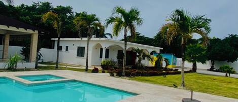 A swimming pool with a tiled deck, a white building with arches, and palm trees.