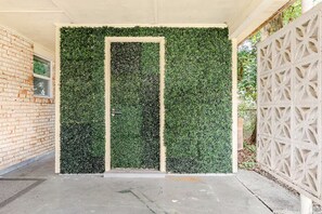 A covered entrance with a green leafy wall, a concrete floor, and a white decorative fence. - Sleeps 14 • 7 Beds • Airport • Navy Base• Hospitals • Mall • Beaches (Pensacola)