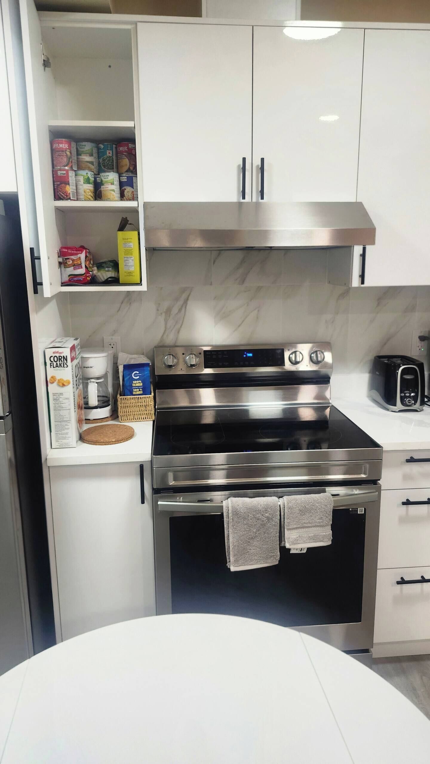Une cuisine équipée d’une cuisinière en acier inoxydable, d’une machine à café et de divers produits alimentaires rangés sur les étagères.