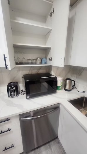 A kitchen with white cabinets, a black microwave, a toaster, a kettle, and a stainless steel sink. - Cozy Bedrooms.  Serene neighborhood. (Fort Saskatchewan)