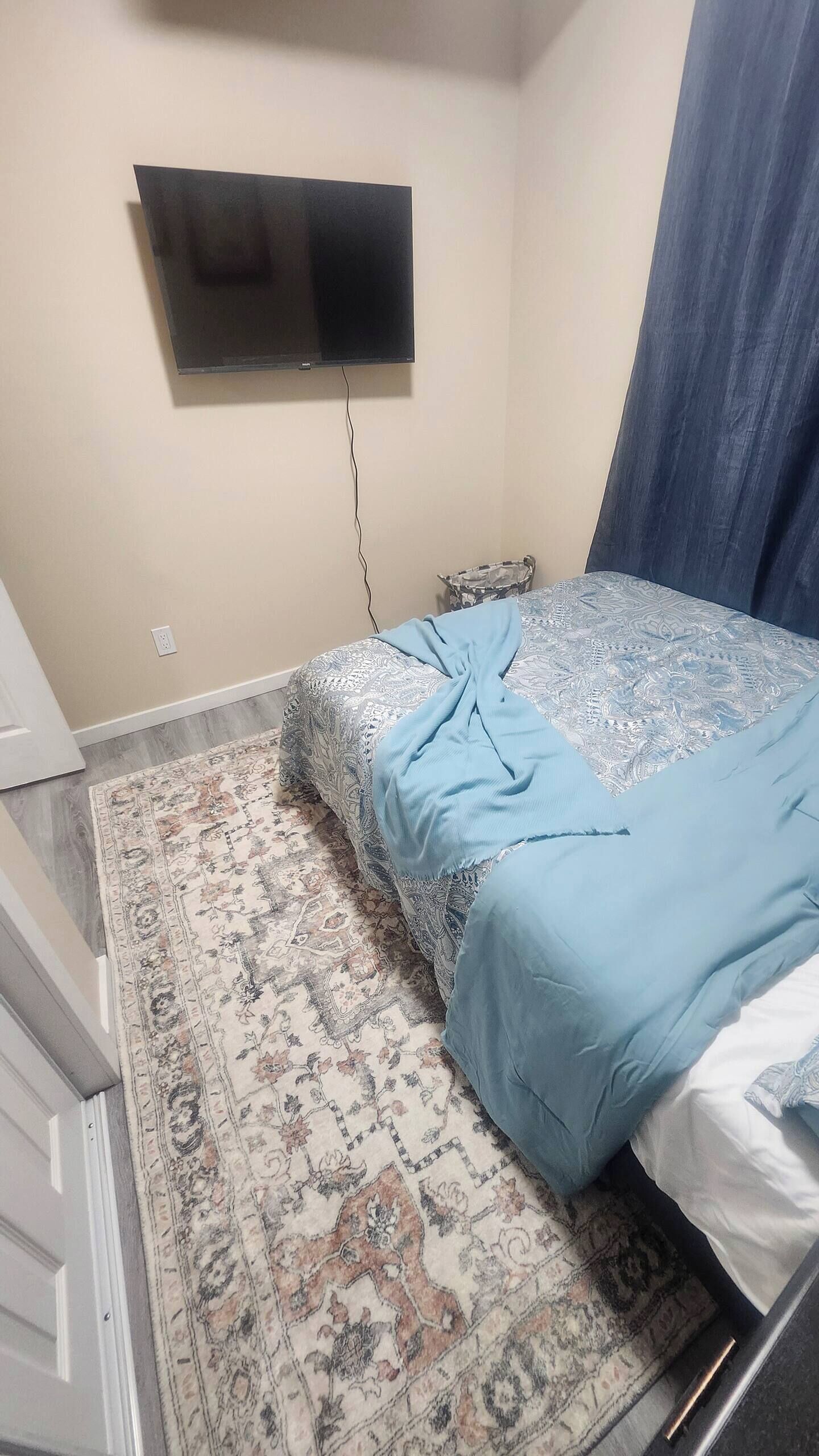 Une chambre à coucher avec un lit, un téléviseur fixé au mur et un tapis à motifs.