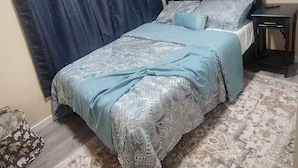 A bedroom with a bed, a nightstand, a rug, and two framed pictures on the wall.