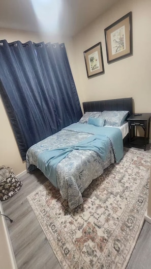 A bedroom with a bed, a nightstand, a rug, and two framed pictures on the wall.