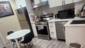 Una cuina moderna amb armaris blancs, electrodomèstics d'acer inoxidable i un sòl de fusta gris.