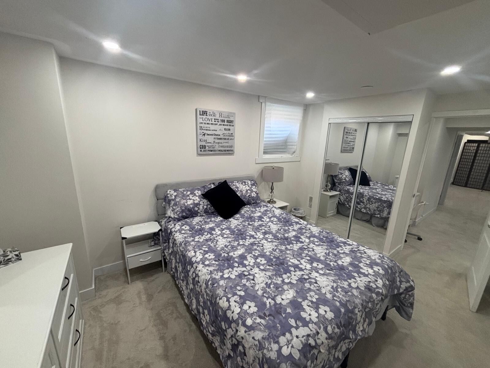 A bedroom with a bed, bedside tables, a mirror, and a wall with motivational quotes.