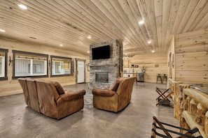L’intérieur d’une cabane en rondins, avec une cheminée en pierre, des fauteuils inclinables en cuir et un coin repas.