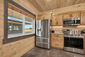 Une cuisine moderne dotée d’appareils électroménagers en acier inoxydable, de meubles de rangement en bois et d’une grande fenêtre.