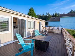 Spacious outdoor deck with turquoise chairs, a fire pit table, and sliding door access. - Enchanting 3BR Soundview | Patio | Firepit | W/D (Camano)