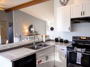Kitchen with white cabinetry, marble-look countertops, and an open layout to the living area. - Enchanting 3BR Soundview | Patio | Firepit | W/D (Camano)