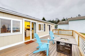 Eine Terrasse mit zwei Adirondack-Stühlen, einem Tisch und einer Schiebetür zu einer Küche.