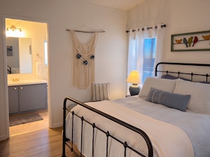 Ein Schlafzimmer mit Bett, Nachttisch, Lampe und Wandbehängen aus Makramee.