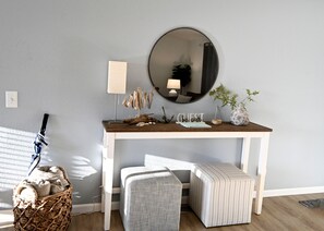 A room with a white console table, a round mirror, a wicker basket, a striped ottoman, and a small plant. - Enchanting 3BR Soundview | Patio | Firepit | W/D (Camano)