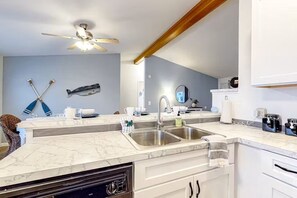 A modern kitchen with a marble countertop, stainless steel sink, and a ceiling fan. - Enchanting 3BR Soundview | Patio | Firepit | W/D (Camano)