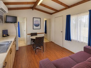 Habitación compacta con kitchenette, comedor con mesa y sillas, un sofá y un ventanal con cortinas.