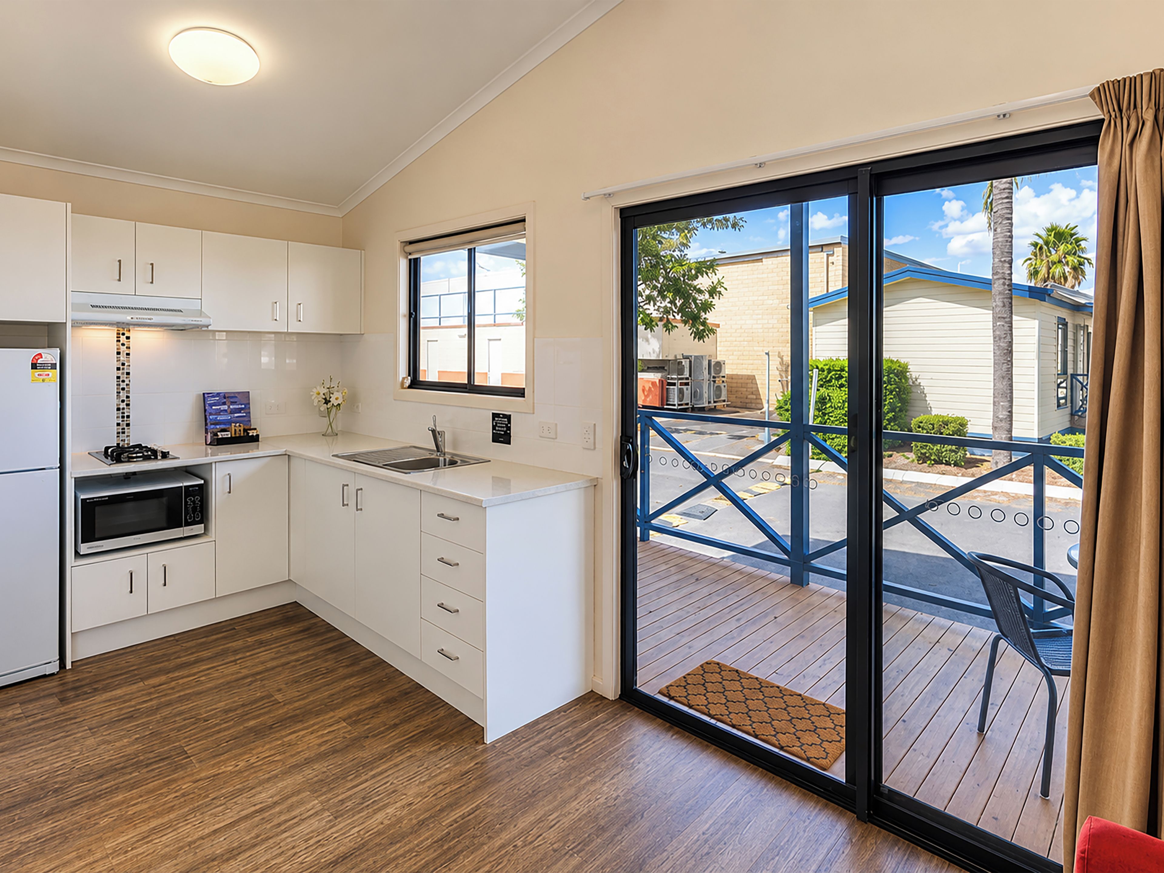 A modern kitchen with white cabinetry, a built-in microwave, and a large sliding glass door leading to an outdoor deck.