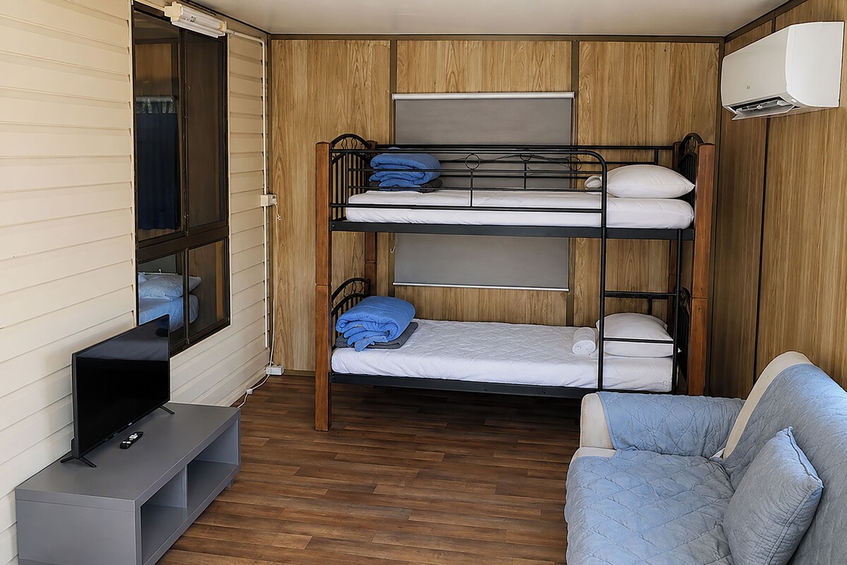 A compact room with bunk beds, a sofa, a TV, and a window.