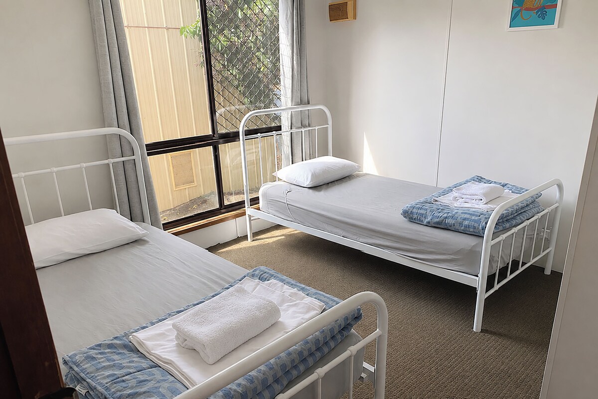 A room with two single beds, each with a pillow and a blanket.