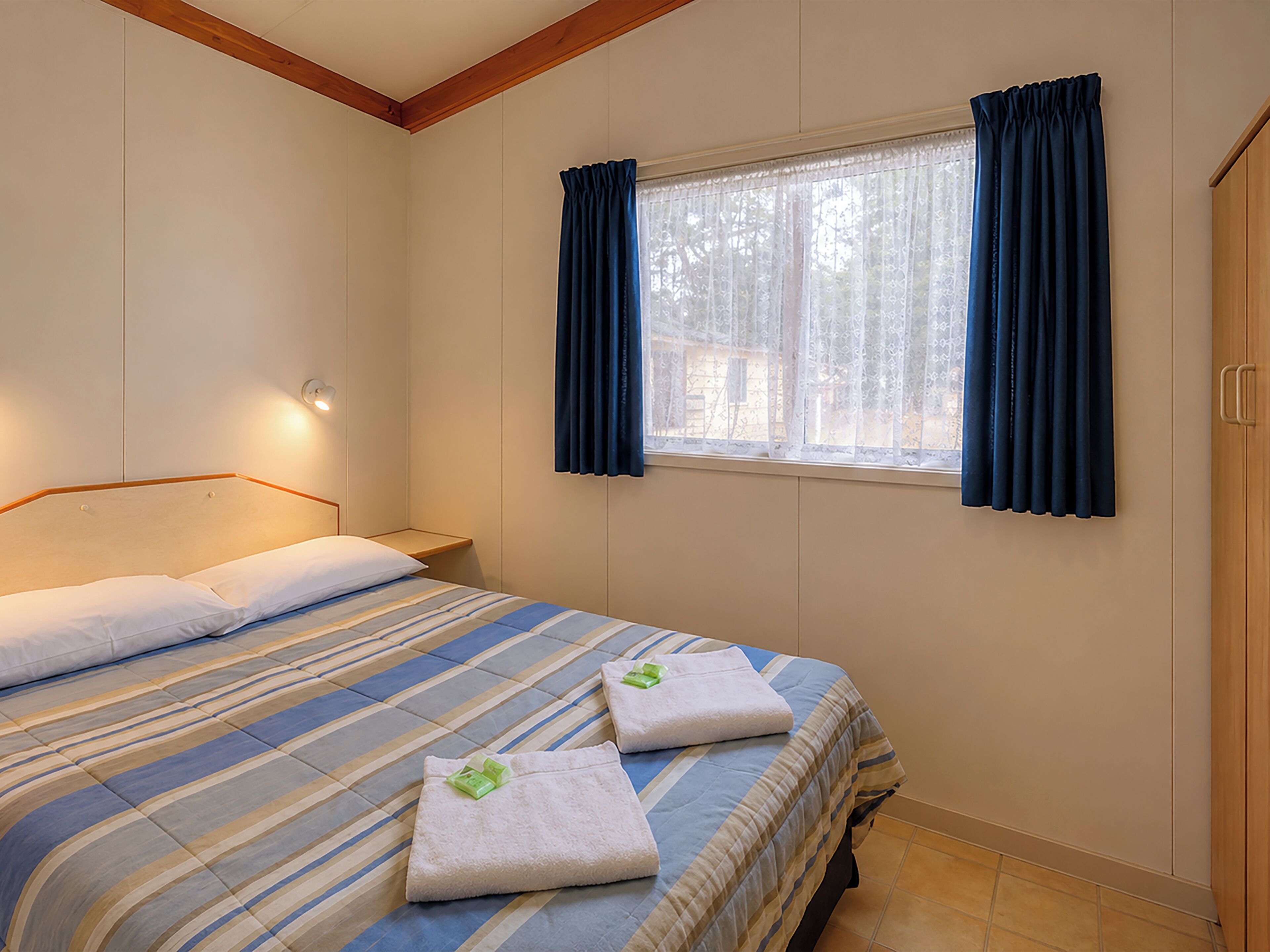 A hotel room with a bed, a nightstand, a window with curtains, and a wardrobe.