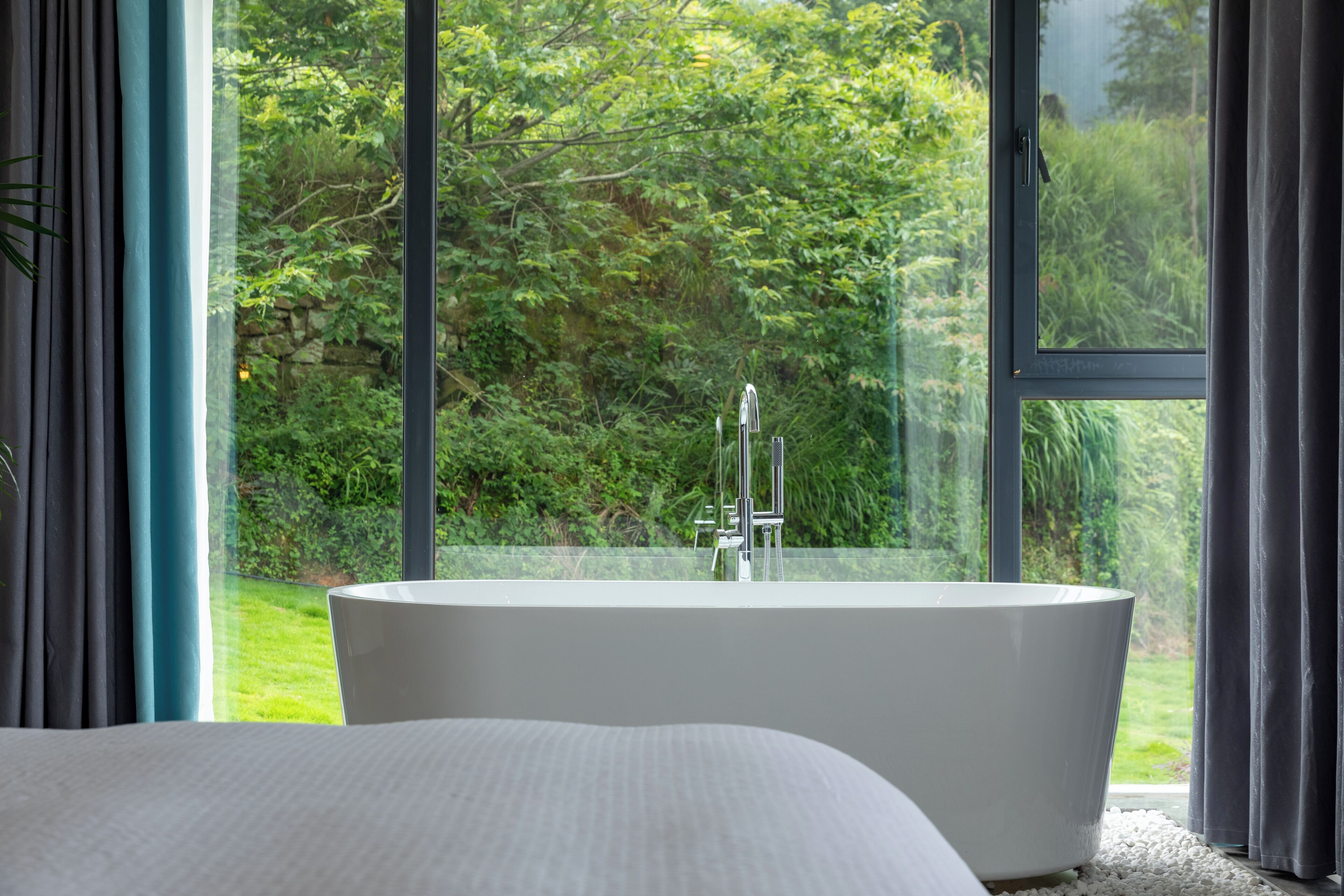 Un baño moderno con una bañera independiente, ventanas amplias y vistas a un jardín exuberante.